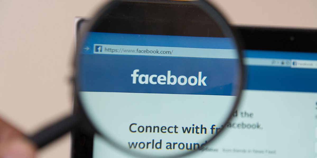 Someone holding up a magnifying glass to the Facebook website Someone holding up a magnifying glass to the Facebook website